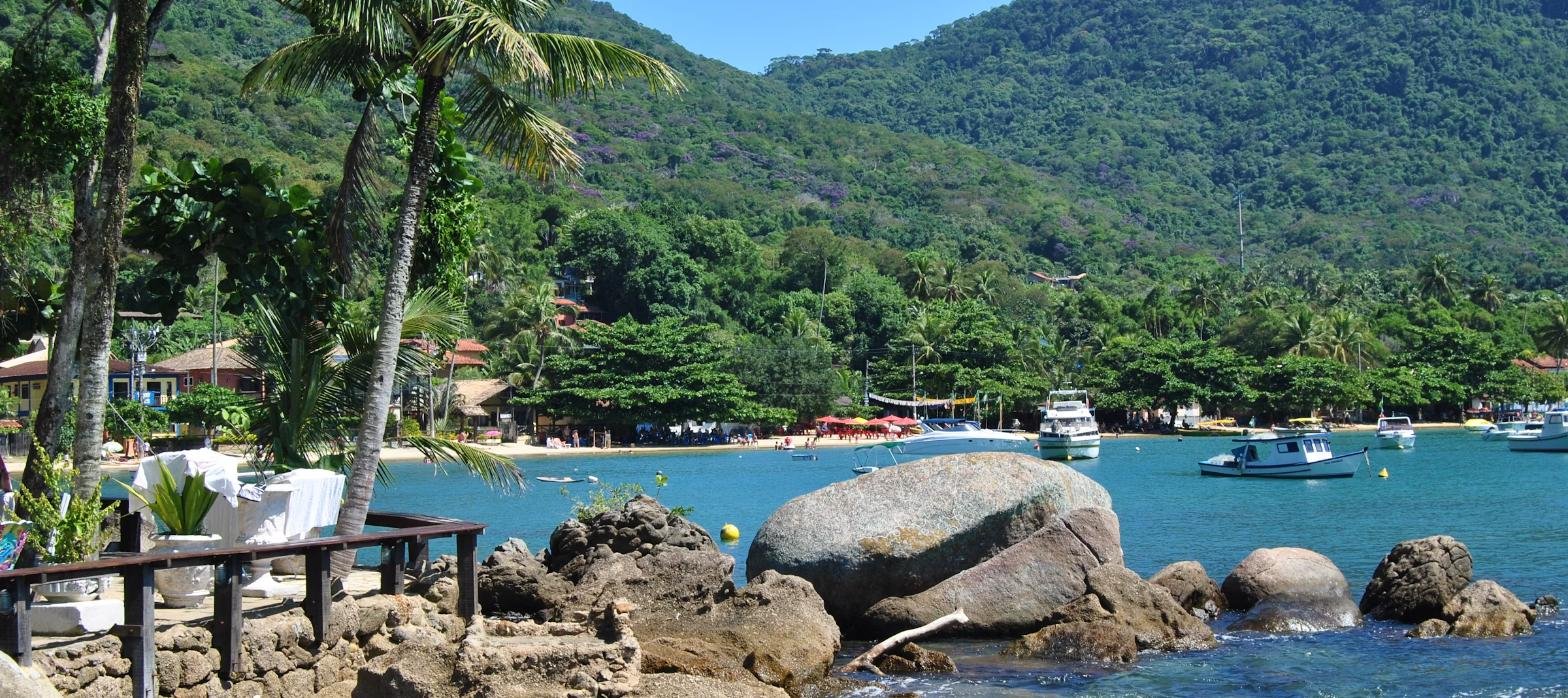 Baía de Angra dos Reis com coqueiros, barcos e serra ao fundo